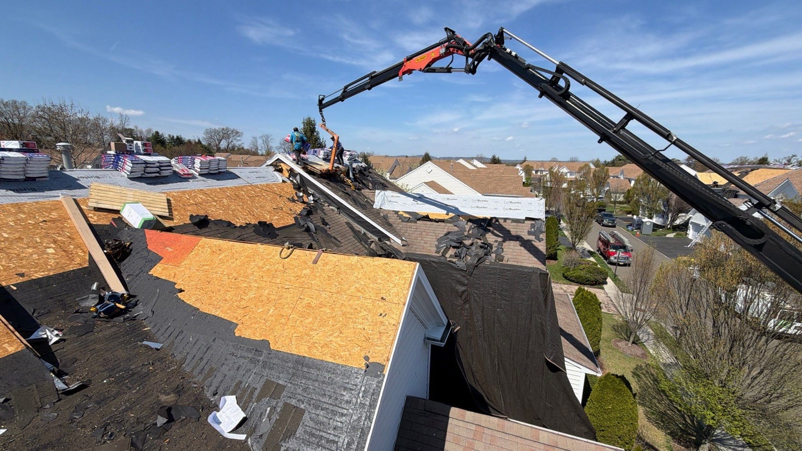Boom crane lifting pallets of GAF shingles onto a large suburban roof